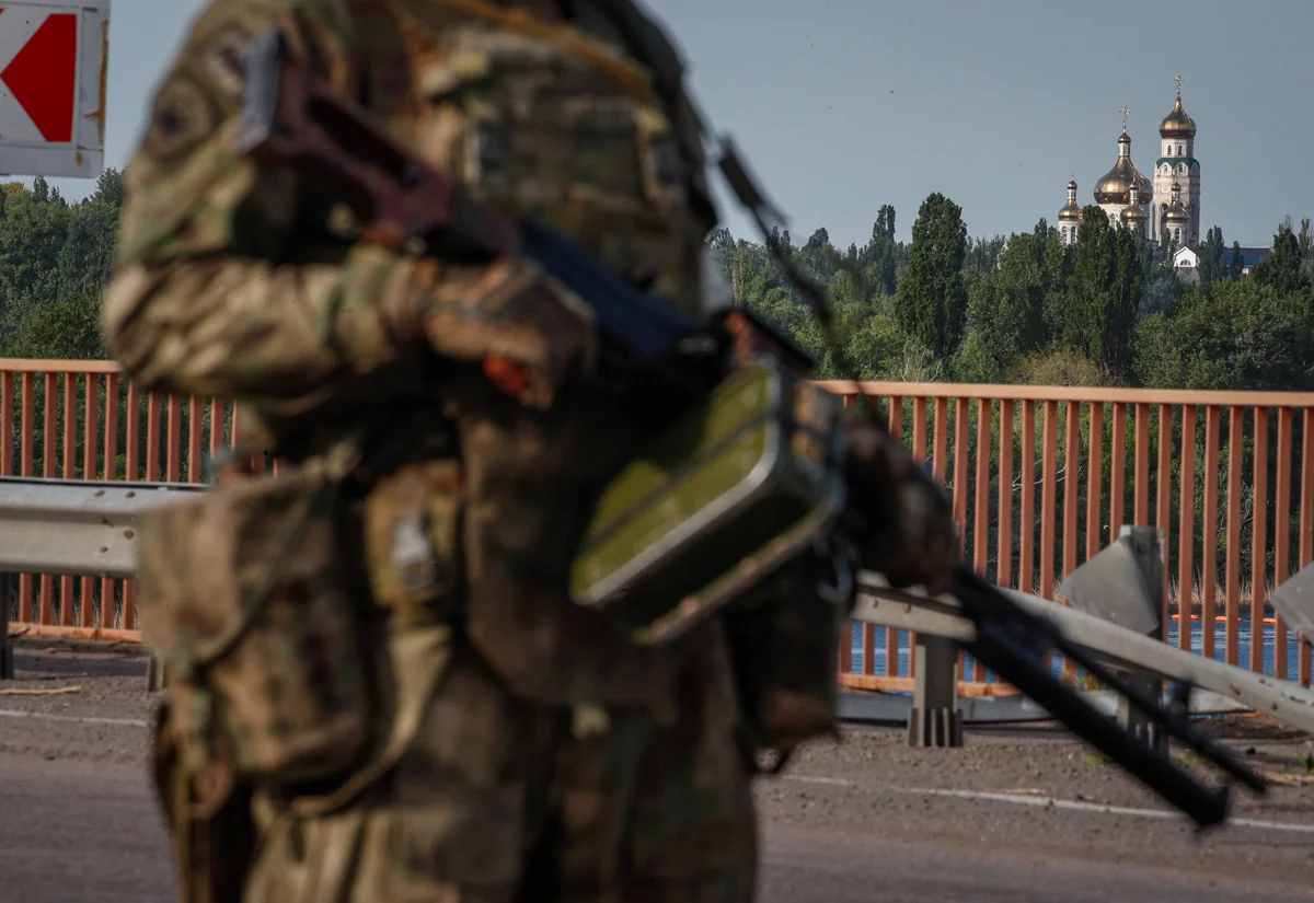 Российский военнослужащий на мосту Каховской ГЭС на фоне православной церкови в Каховке, Украина, 20 мая 2022 года. Фото: Сергей Ильницкий / EPA