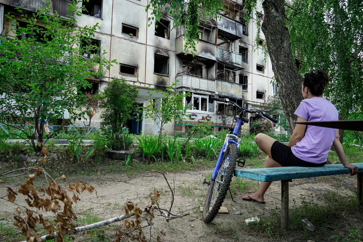 A woman sits in front of a burnt-out apartment block in the Belgorod region town of Shebekino, in western Russia, 2 July 2023. Photo: EPA