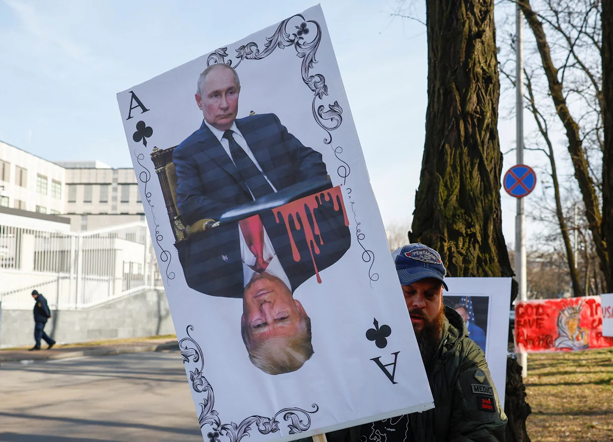 Участник акции держит баннер в виде игральной карты с портретами Путина и Трампа у посольства США в Киеве, 8 марта 2025 года. Фото: Valentyn Ogirenko / Reuters / Scanpix / LETA